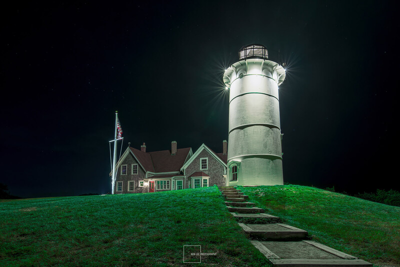 Illuminated lighthouse and keeper's house on green hillside at night