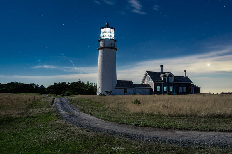 White lighthouse tower with keeper's house on rural grassland under blue sky