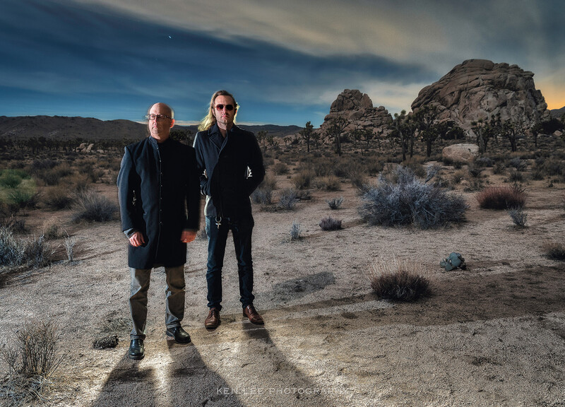 Two men standing in desert landscape with rock formations at golden hour