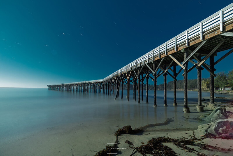 Long wooden pier extending into calm turquoise ocean water under clear blue sky