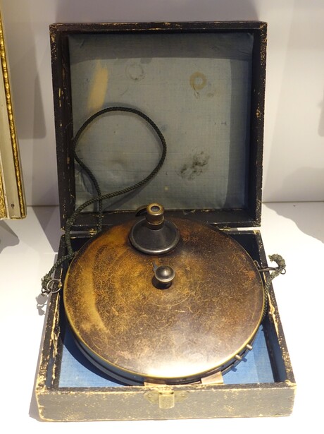 A concealed  waistcoat  spy camera of the 1880s, the flat round type worn under a coat with its lens poking through a buttonhole
