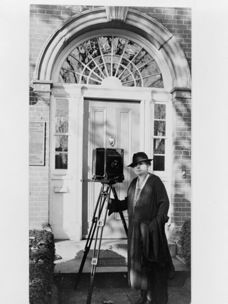 Frances Benjamin Johnston with a view camera on a tripod outside a doorway, photographed around 1935, when she was in her late sixties and deep into the Carnegie Survey