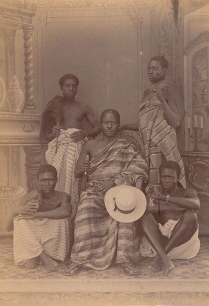 Five men photographed around 1880 in the Accra studio of the Lutterodts, among West Africa's earliest professional photographers, posed against a painted backdrop with borrowed cloth and props