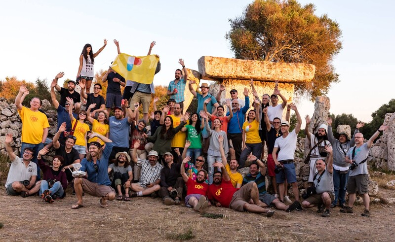 Large group of people in yellow and blue shirts posing together outdoors with hay bales
