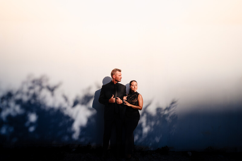 Couple in formal attire silhouetted against dramatic sky with mountains