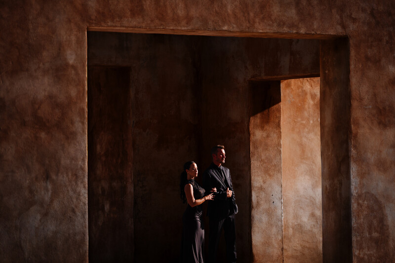 Two people standing in a minimalist interior with warm-toned concrete walls and geometric architectural elements