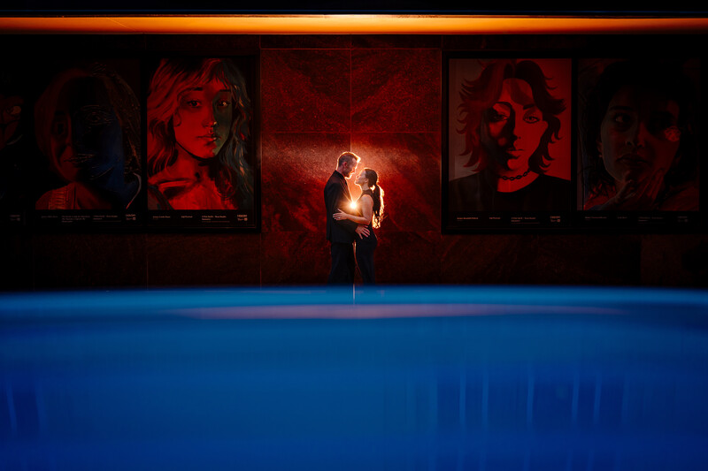 Two figures illuminated by warm light against dark backdrop with red portrait panels