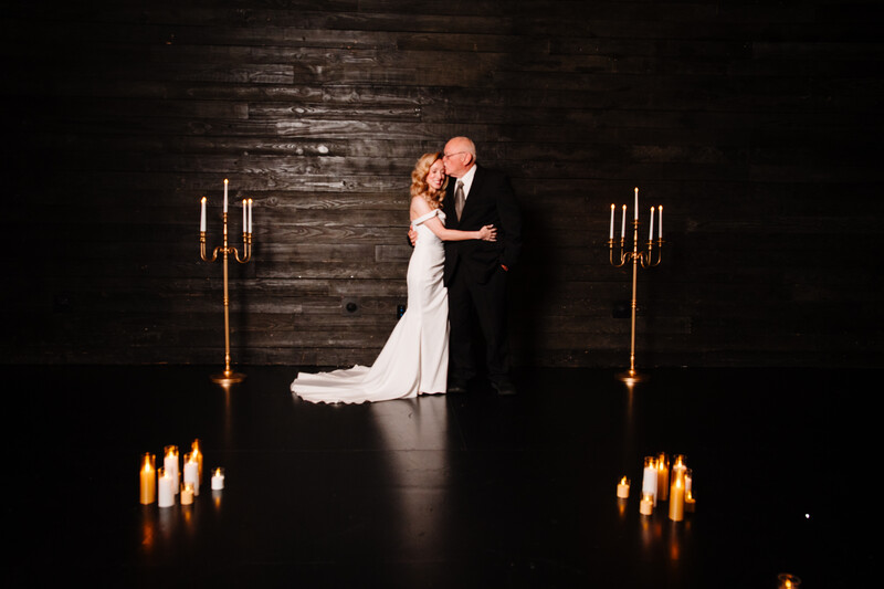 Bride and groom first dance illuminated by candles against dark wooden backdrop