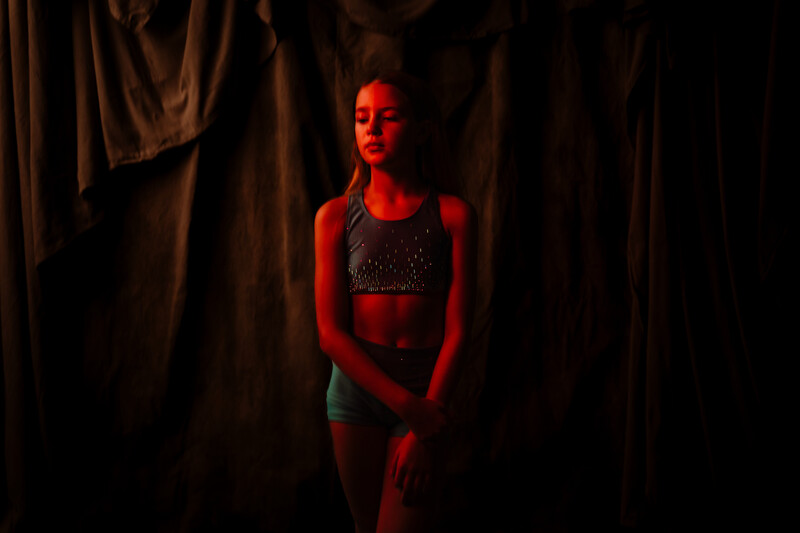 Female subject illuminated by red gel lighting against dark draped fabric backdrop