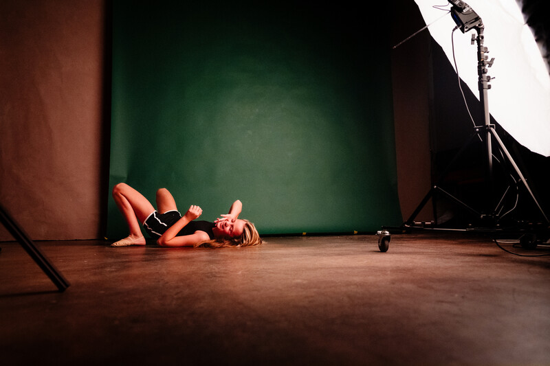 Model lying on studio floor in orange clothing under dramatic studio lighting with green backdrop