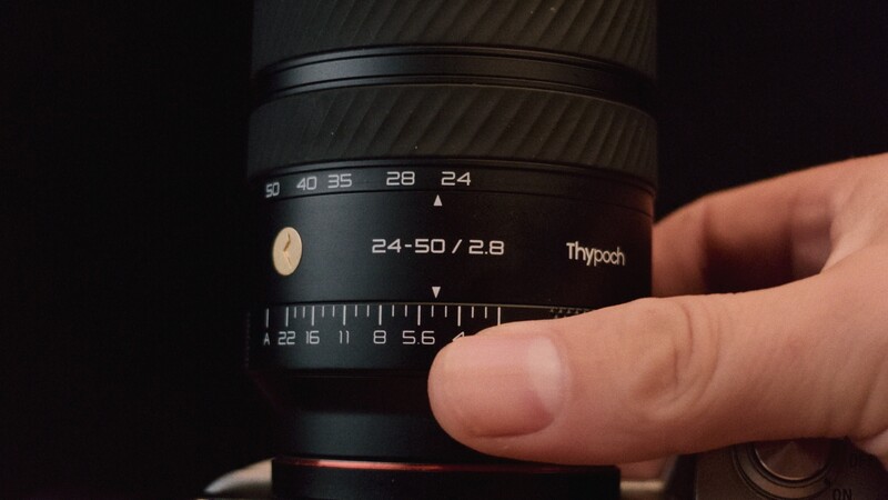 Hand adjusting focus ring on Thypoch 24-50mm f/2.8 lens showing aperture and focal length markings