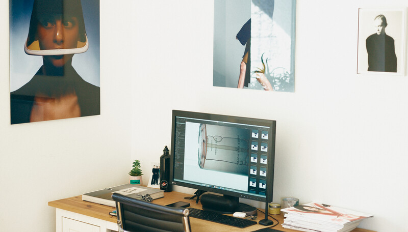 Creative workspace with desktop monitor displaying design software, surrounded by portfolio prints on white wall