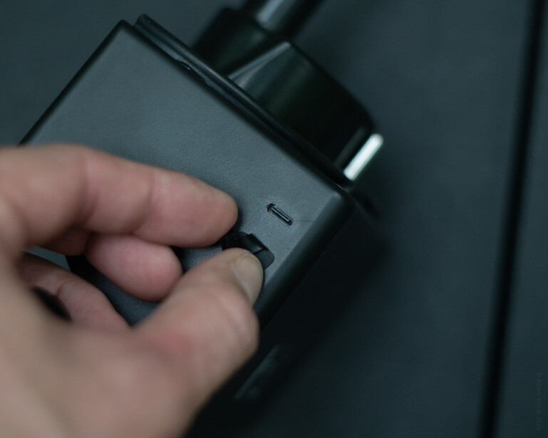 Hand holding a compact camera gimbal or stabilizer with attached lens against a dark background