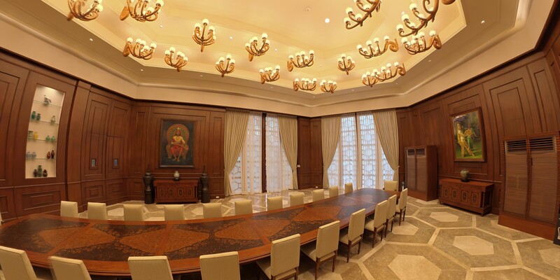 Elegant conference room with curved wooden table, cream chairs, ornate ceiling fixtures, and warm ambient lighting
