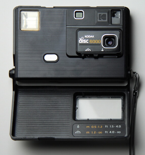 A Kodak Disc 6000, its film door swung open, showing the flat card-deck body, the small fixed lens, and the built-in flash