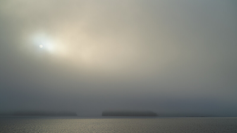 Misty seascape with sun breaking through heavy fog and distant landmasses