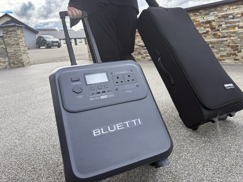 Bluetti portable power station with rolling handle and black carrying cases on residential driveway