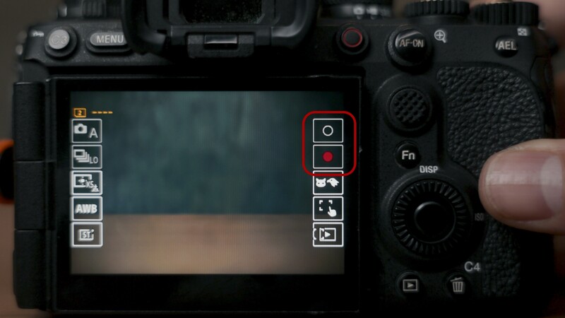Sony mirrorless camera rear LCD screen displaying menu interface with hand adjusting control dial