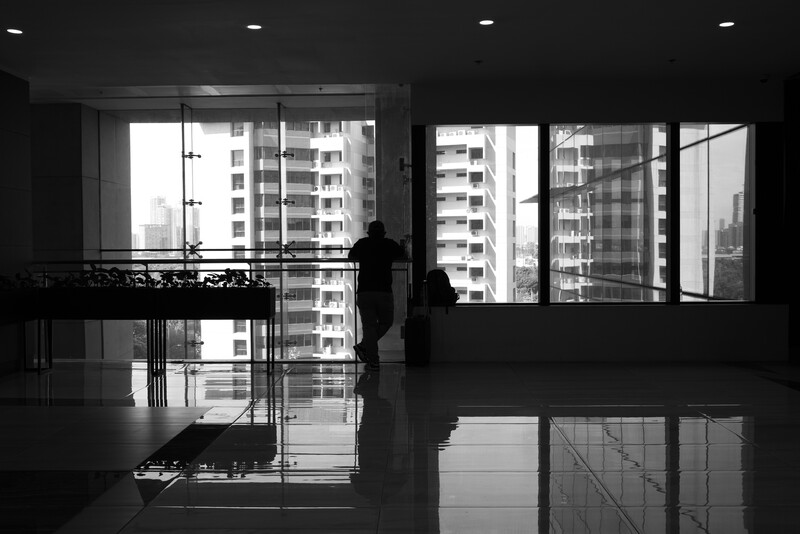 Silhouetted figure standing in a modern high-rise interior with floor-to-ceiling windows overlooking residential buildings