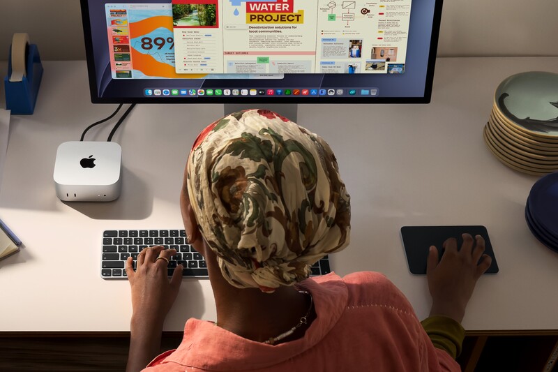 Person wearing camouflage beanie at desk working on keyboard and touchpad with Mac mini and monitor