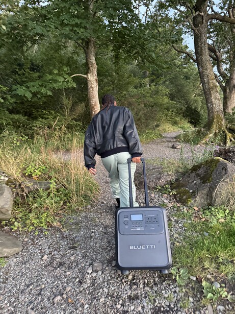 Photographer walking away on gravel path carrying rolling suitcase with camera gear