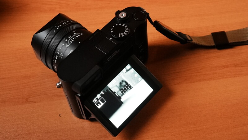 Black mirrorless camera with articulating LCD screen and manual focus lens on wooden surface