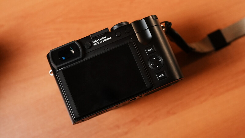 Black compact digital camera with LCD screen displayed on warm orange wooden surface