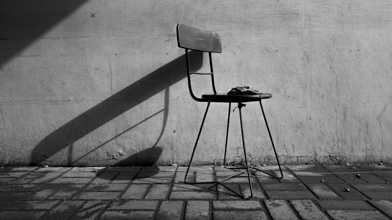 Minimalist black and white photograph of a simple metal chair casting a dramatic shadow on a concrete wall