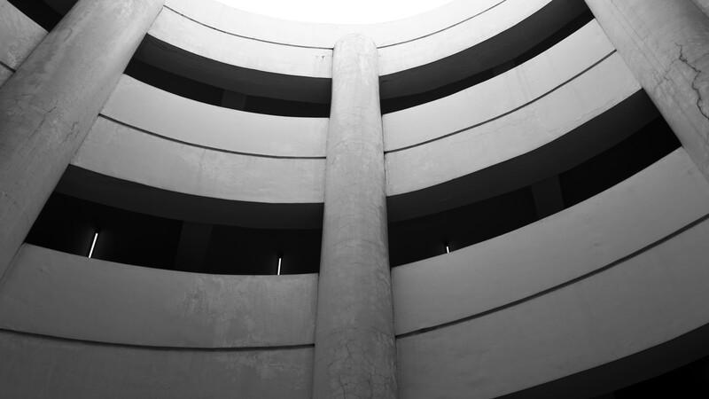 Concentric circular bands of a brutalist concrete structure shot from below in black and white