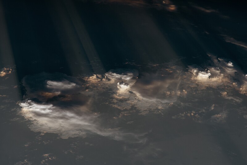 Crepuscular rays photographed from the International Space Station, looking down on cumulonimbus towers casting shadow corridors across the cloud deck