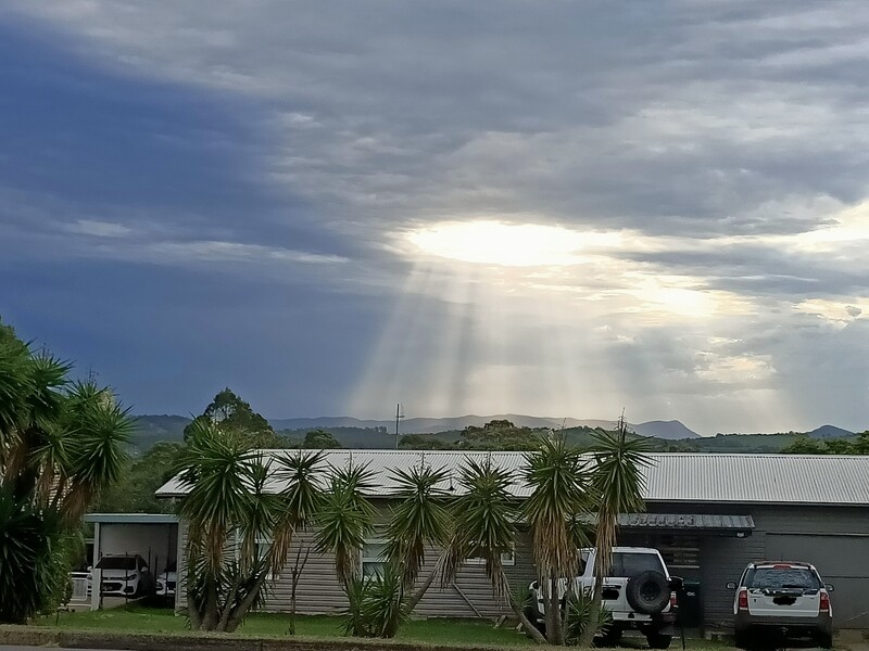 Sunlight through a gap in dark storm cloud, scattering off haze so the lit corridors read as solid beams against the shadowed sky