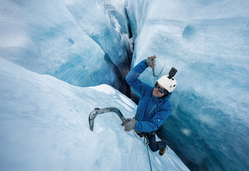 Ice climber ascending a crevasse wall on a glacier, wearing blue jacket and white helmet