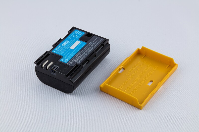 An LP-E6N with the plastic terminal cover that keeps the contact block from shorting against keys or coins in a bag