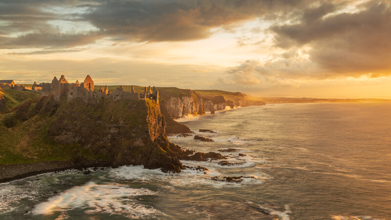 Medieval castle ruins on dramatic coastal cliffs at golden hour