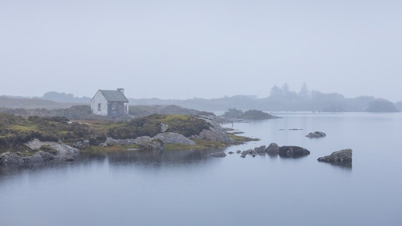 Isolated house on rocky coastal island surrounded by still water in heavy fog