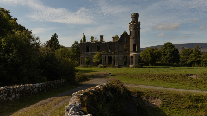 Abandoned stone mansion with tower in overgrown landscape