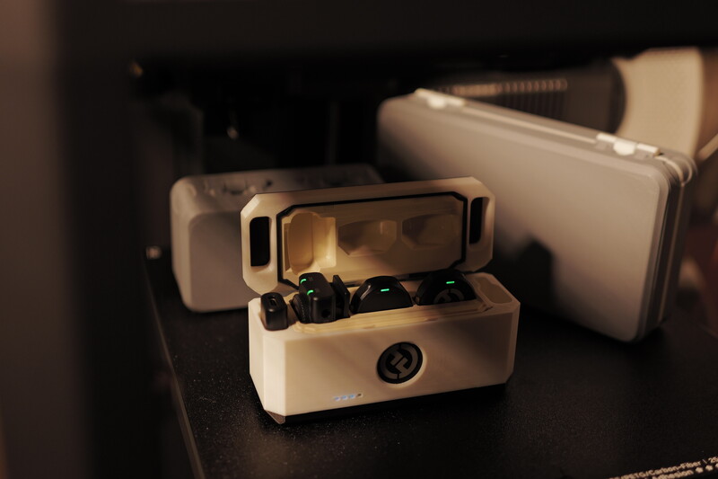 White wireless earbuds charging case with buds visible inside, positioned among matching white storage boxes on dark surface