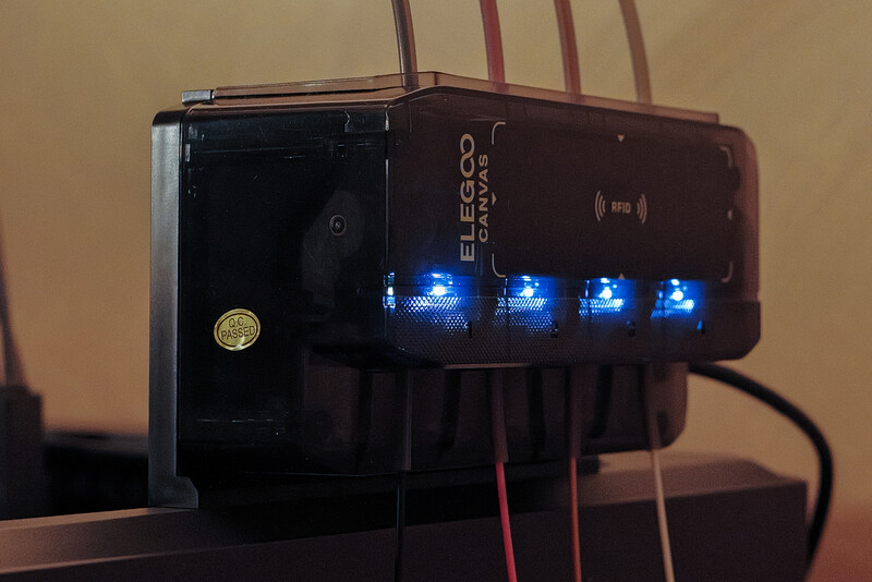 Elgato power hub with four illuminated blue LED indicator lights and connected cables against warm wall background