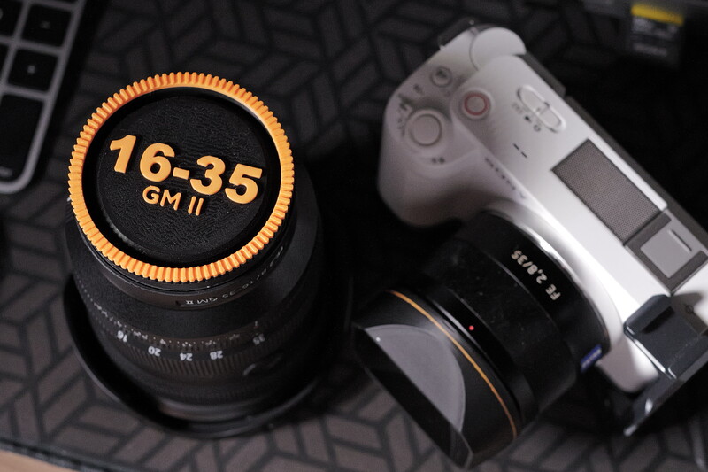 A 16-35mm GM lens with orange markings next to a Sony mirrorless camera body on a patterned surface