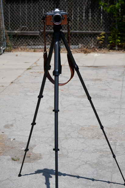 Vintage film camera mounted on black tripod in outdoor concrete setting