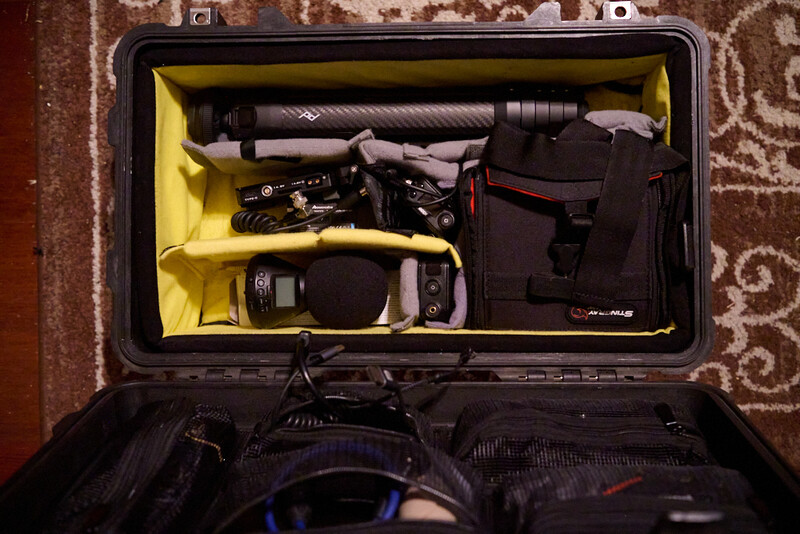 Open camera equipment case with organized gear including lenses, camera body, and accessories in yellow foam padding