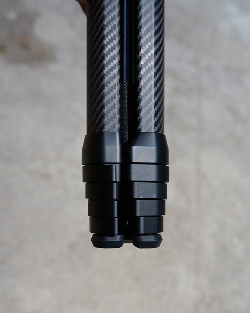 Two carbon fiber tripod legs with black connectors viewed from above against concrete background