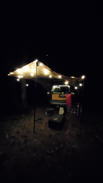 Illuminated tent with string lights at night, vehicle parked underneath