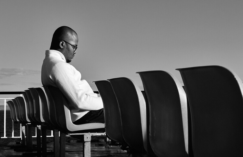 Man in white shirt seated among stacked black chairs in black and white composition