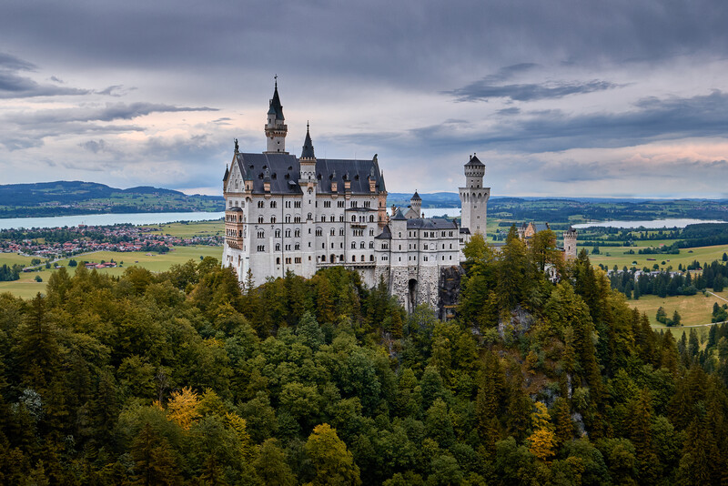 Neuschwanstein Castle perched on a forested hilltop with Alpine valley landscape beyond