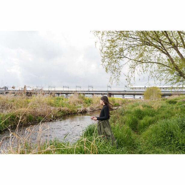 Photographer standing by a shallow stream with camera, industrial bridge and overcast sky in background