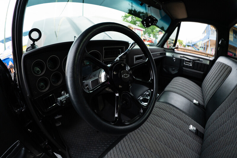 Interior of a classic truck with black steering wheel, dual instrument cluster, and gray striped bench seat