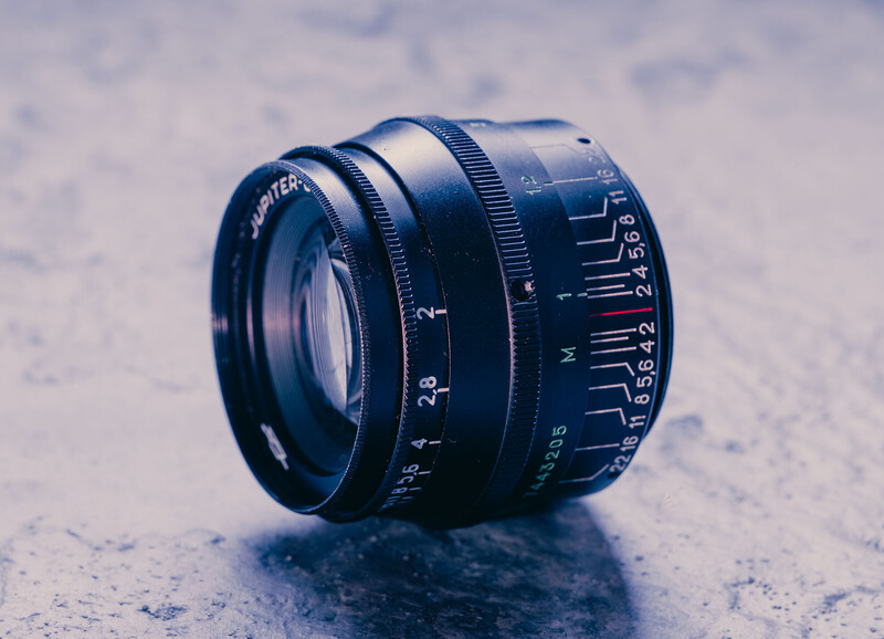 Vintage rangefinder lens with manual focus ring and aperture markings on textured surface