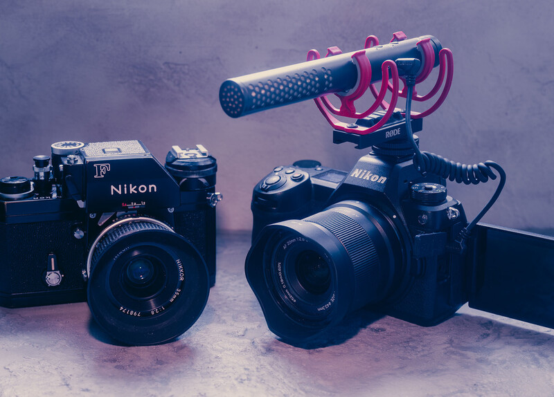 Two Nikon cameras with a pink shotgun microphone mounted on a boom arm against a purple backdrop