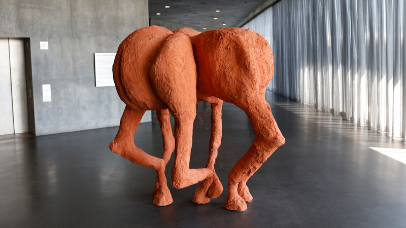Large terracotta-colored sculptural form of an abstract figure in a minimalist gallery space
